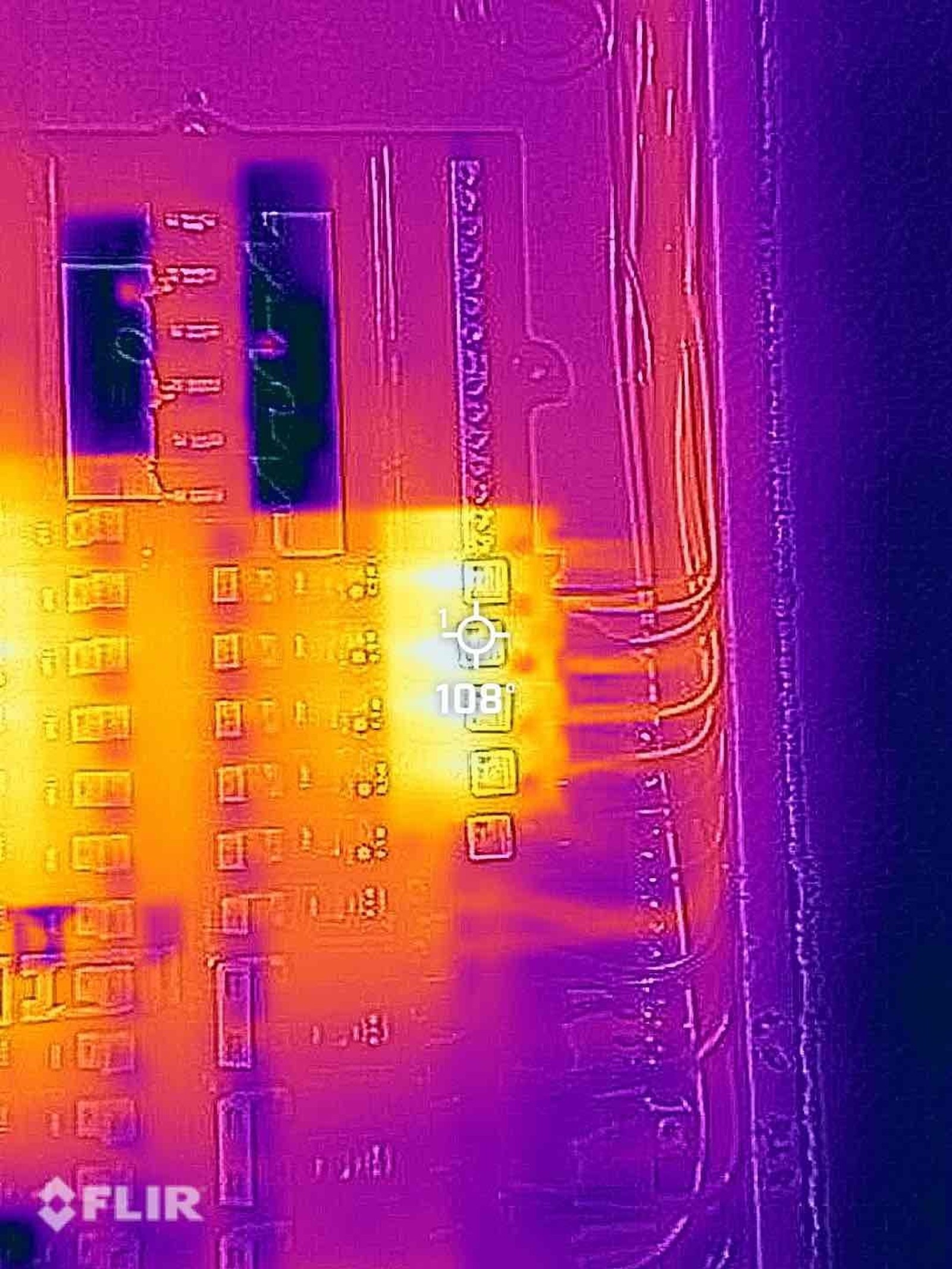 FLIR thermal image of wall-mounted switch and outlet showing severe heat signature at central outlet location indicating potential backstabbed connection resistance.
