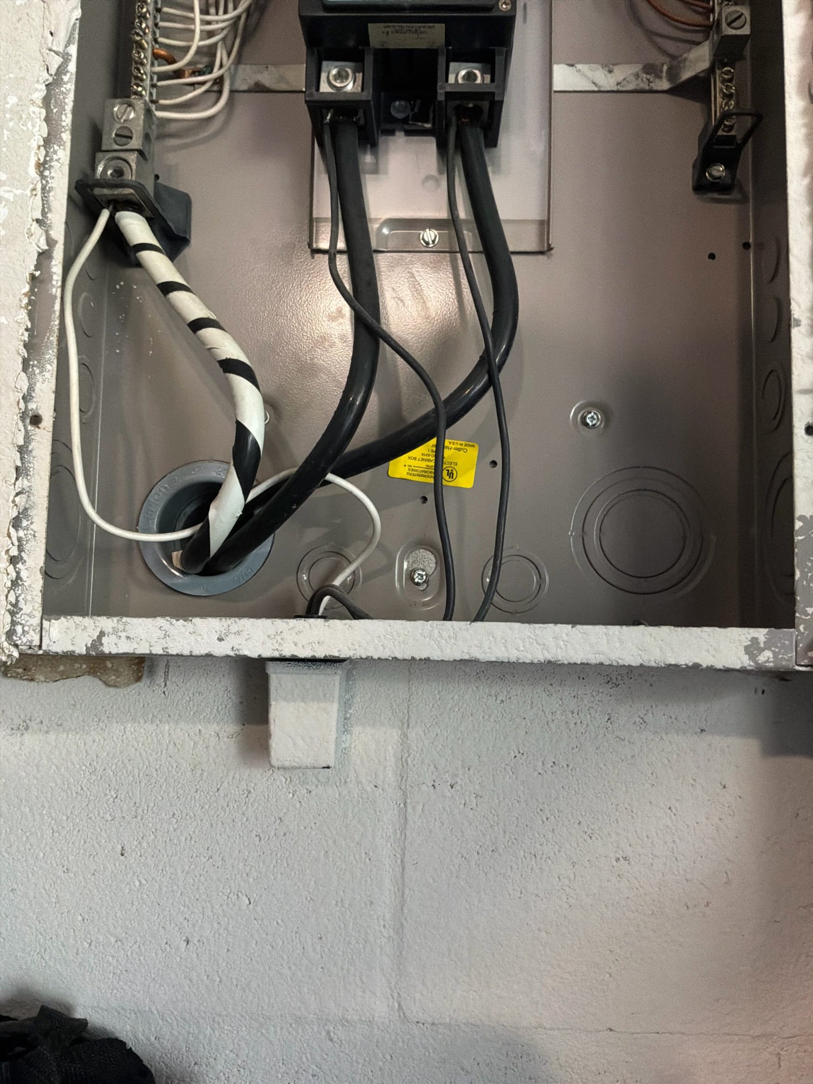Sub-panel exterior installation showing multiple wires entering through knockouts without proper 2-inch bushings, with loose and crossing service conductors.