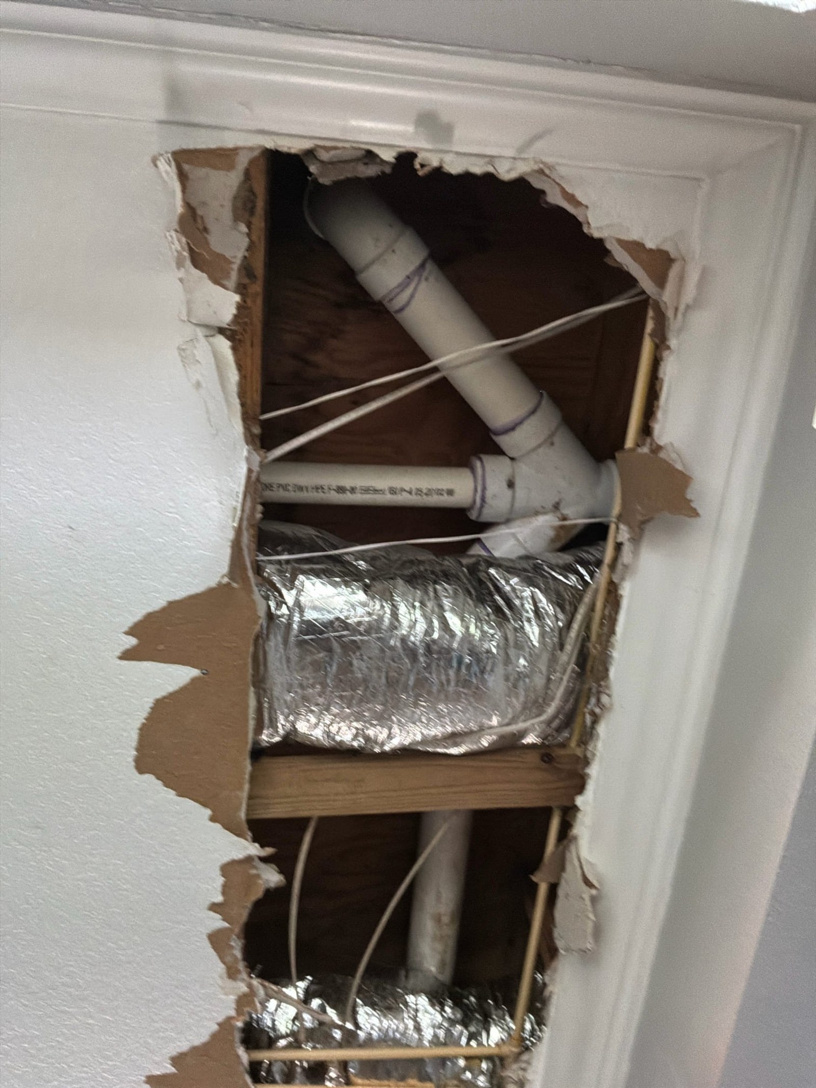 Rough-in wiring in wall cavity showing unprotected PVC conduit and bare wires with foil-wrapped insulation, lacking proper cable connectors and strain relief.