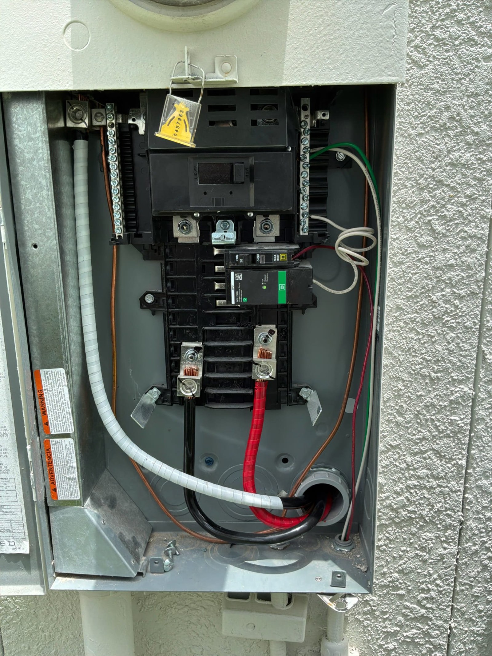 Electrical subpanel interior showing main breaker, circuit breakers, and feed wires with protective conduit.