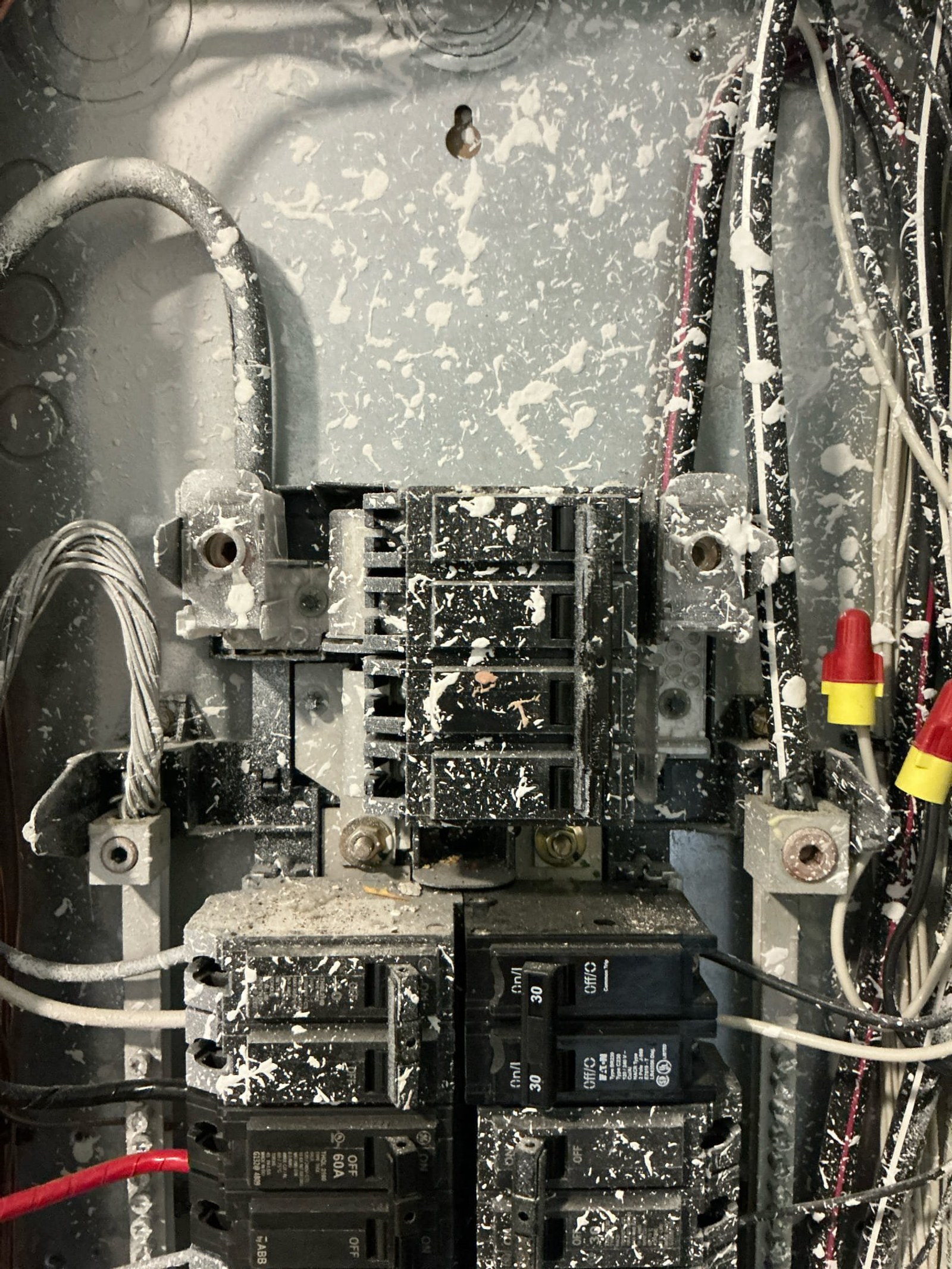 Panel interior close-up showing corroded main breaker area and tangled white conductor wires with improper connections and visible terminal damage.