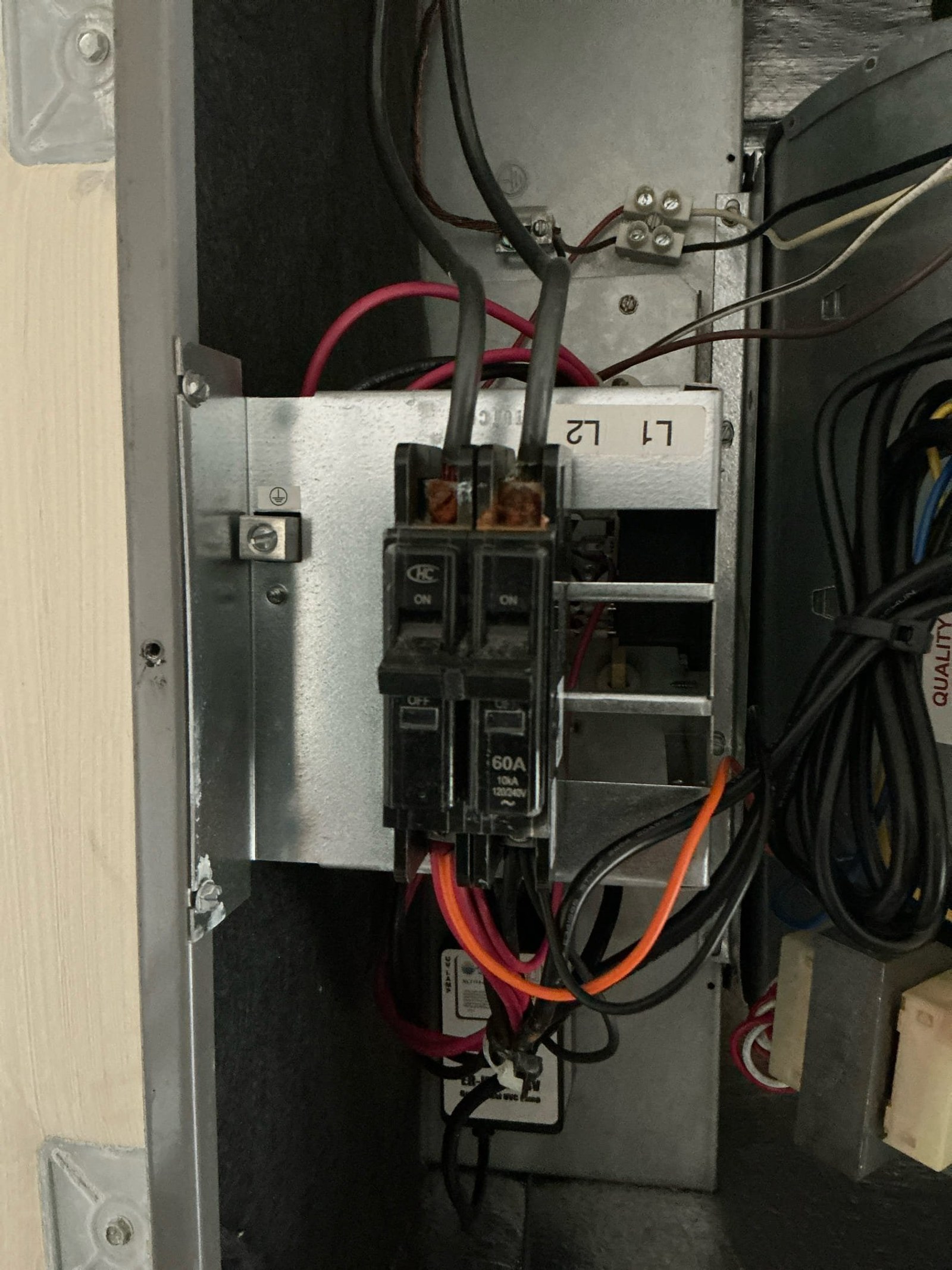Sub-panel or disconnect with two 60-amp breakers, red and orange conductors connected to terminals, showing inadequate grounding connection.