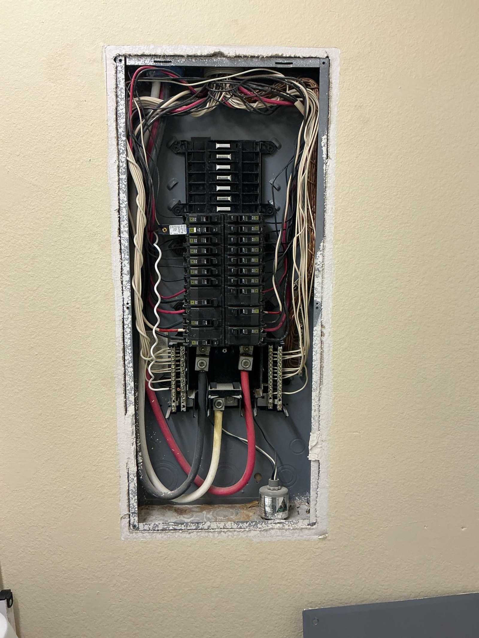 Sub-panel interior with tangled wiring and multiple conductors looped around terminals showing poor wire management and code violations.