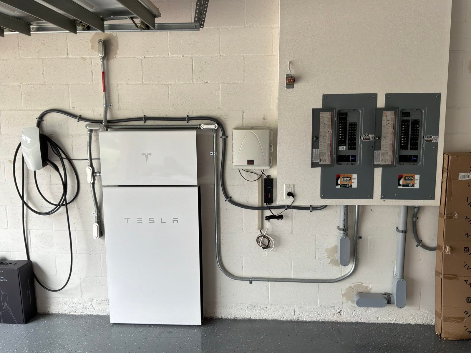 Completed EV charging installation with Tesla Powerwall battery storage system and two sub-panels mounted on wall with proper conduit routing.