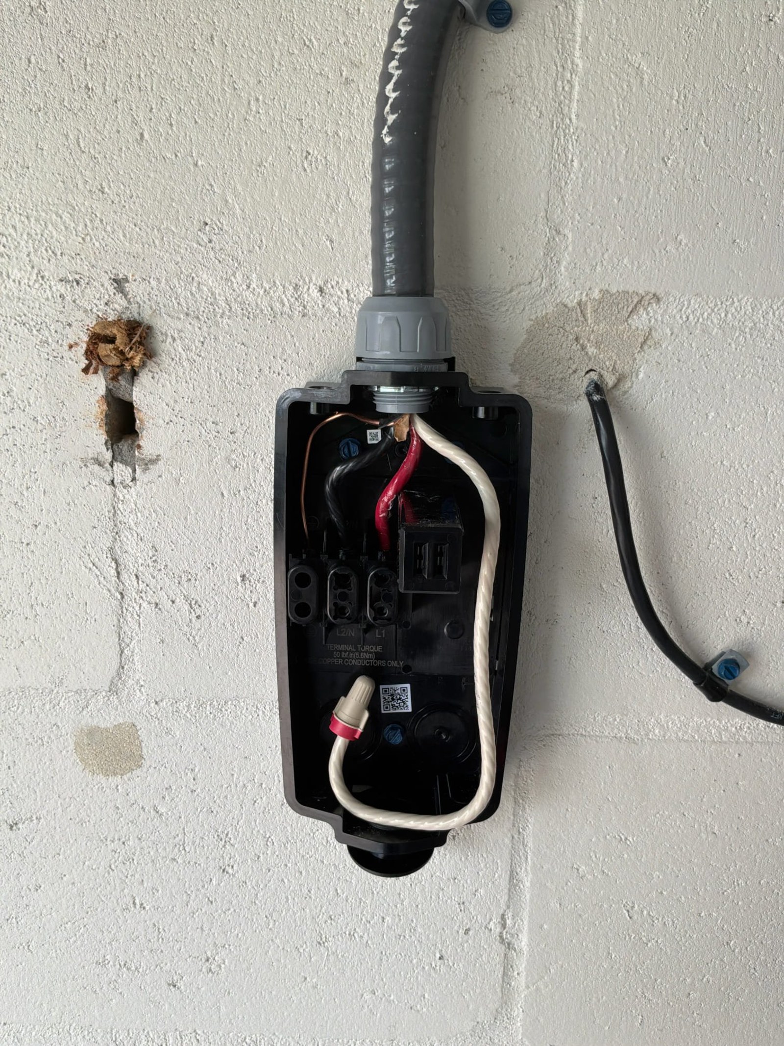 Outlet box interior showing backstabbed wires pushed into spring terminals without proper strain relief on a wall-mounted outlet.