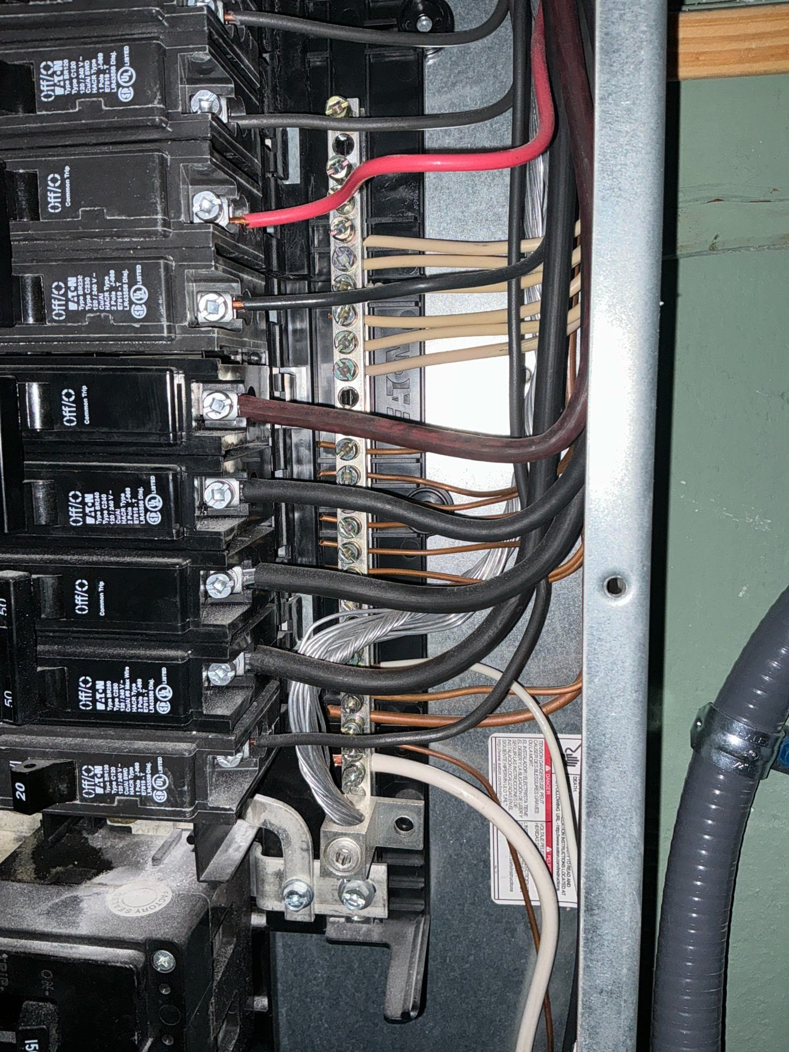 Panel interior close-up showing multiple breakers with black and tan wires routed to terminal blocks, including red and black conductors with improper wire management and no clear circuit organization.