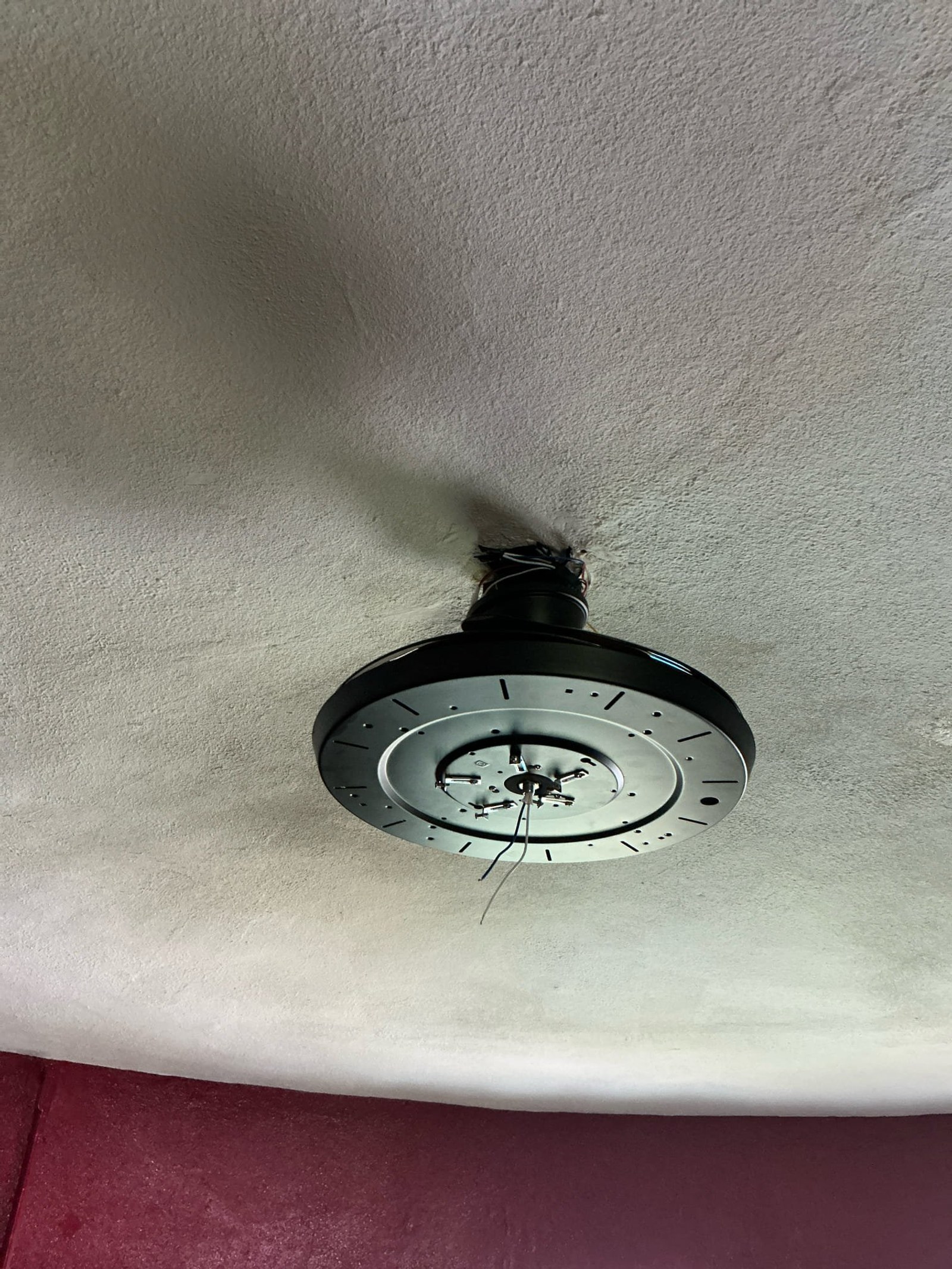 Ceiling-mounted light fixture with bare wires exposed at connection point prior to fixture installation.
